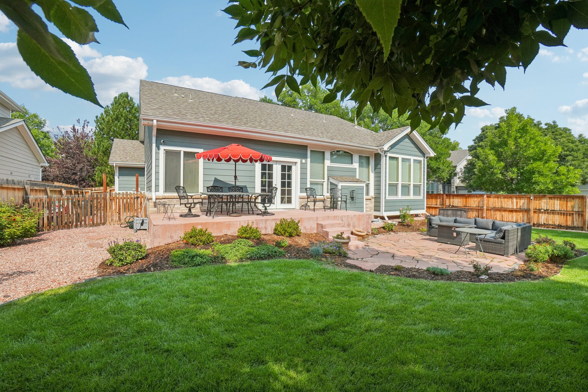 Back exterior view of Aurora ranch home at 762 Helena St featuring patio seating, red umbrella, and landscaped backyard.